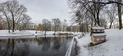 Panoramic winter landscape with snow in park with canal in Riga, Latvia. View of small house for birds snow covered park.
