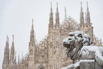 The facade of the famous Milan Cathedral under a heavy snowfall. Lion statue in the foreground.