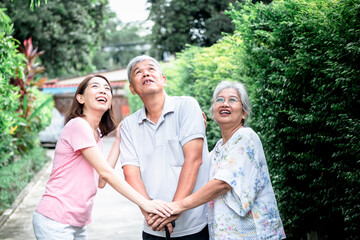 Fototapeta premium Asian family, an elderly couple and a daughter, They are looking up and all holding hands to encourage each other, concept to relationship and health care in family.