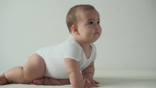 infant, childhood concept - happy funny playfull toddler kid 8 month baby girl learn to sit singly play on bed. smiling chubby active awake newborn crawl on knees indoors at home on white background