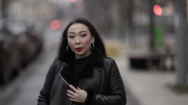 Front view of a beautiful and spectacular Asian woman with red lipstick on her lips in a stylish image walking along a daytime city street in the background, she walks and poses.