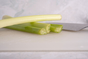 Green Celery Being Sliced on White Cutting Board With Chef's Knif and Wood Stand