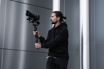 Young Professional videographer holding professional camera on 3-axis gimbal stabilizer. Pro equipment helps to make high quality video without shaking. Cameraman wearing white hoodie making a videos. © Volodymyr_sh