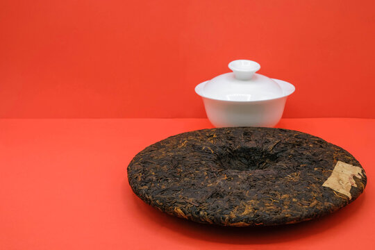 Round flat disc of puer tea and porcelain gaiwan. Red background. Minimalism. Copy space.
