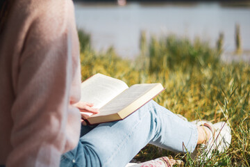 close up shot of a woman reading a book in a park next to the river, beautiful view, relax concept
