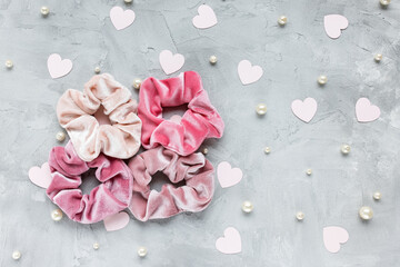 Four trendy velvet scrunchies, pastel pink paper hearts and white pearls on gray background. Diy accessories and hairstyles for Valentines Day, fashion and lifestyle concept, copy space