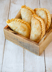 Fried beef patties or pies inside wooden box on rustic white wooden table