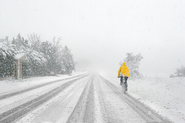 Man riding a bike with yellow jacket on snowy road during a snow storm