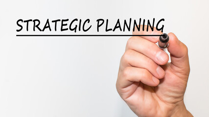 the hand writes text STRATEGIC PLANNING with a marker on a white background. business concept