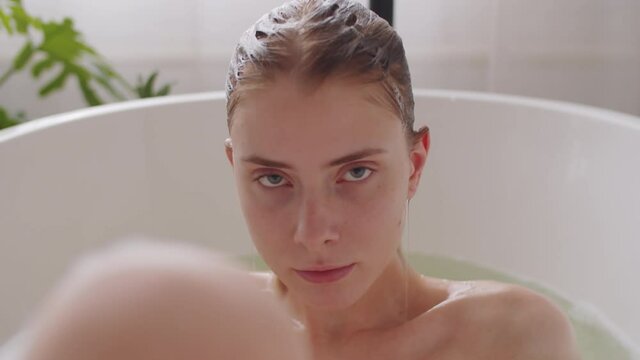 Close up portrait shot of young attractive caucasian woman lying in bath water, then getting out of it and looking at camera seductively
