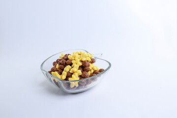 A glass bowl filled with chocolate and corn cereal isolated on the yellow background