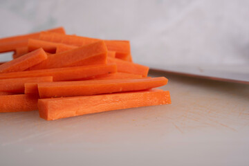 Carrots being Sliced on White Cutting Board With Chef's Knife and Wood Stand