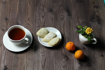 cup of tea, tangerine, yellow rose flower in wase and cookies on brown wooden background
