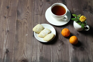 Sweet cookies on plate, cup of tea, tangerine, yellow rose flower in wase  on brown wooden background