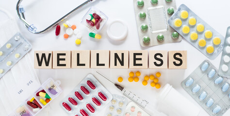 WELLNESS. Medicine word on wooden blocks on a desk. Medical concept with pills, vitamins, stethoscope and syringe on the background.