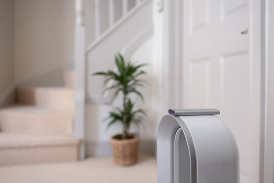 Shallow Focus Of A Floor Standing Air Purifier And Its Controller Seen Atop The Fan Area. The Background Shows A Modern Room And Stairway Leading To The First Floor.