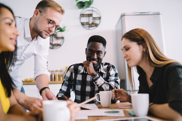 Diverse young coworkers discussing new project while sitting in kitchen interior
