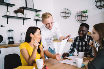 Concentrated young colleagues working with papers at table in kitchen