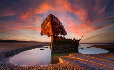 Obraz premium Shipwrecked off the coast of Ireland, An shipwreck or abandoned shipwreck,,boat Wreck Sunset light at the beach, Wrecked boat abandoned stand on beach or Shipwreck