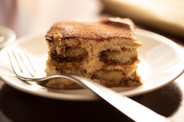 Slice of Traditional Italian Tiramisu on White Plate and Wooden Table with Fork and Coffee Cup.