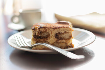 Slice of Traditional Italian Tiramisu on White Plate and Wooden Table with Fork and Coffee Cup.