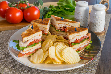 Fresh turkey club sandwich sliced on plate with potato chips