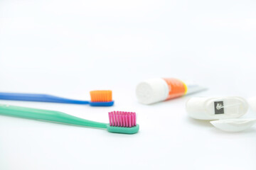 Two colored toothbrushes with bright bristles on the left and a tube of paste and dental floss on the right on a white background, daily oral care