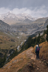 Hiker observing a valley with a river and snow-capped mountains. Ordesa y Monte Perdido Natural Park in the Pyrenees