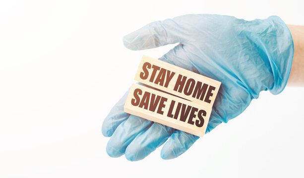 Doctor's hand in blue glove shows the wooden cubes with text "STAY HOME SAVE LIVES". COVID-19 prevention measures.