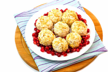 On a white plate, boiled chicken meatballs with chopped walnuts, decorated with pomegranate seeds.