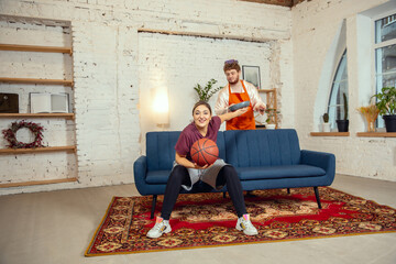 Gender stereotypes. Wife and husband doing things unusual for their genders in social meanings, sense. Man cooking dinner while woman training in basketball with the ball in living room.