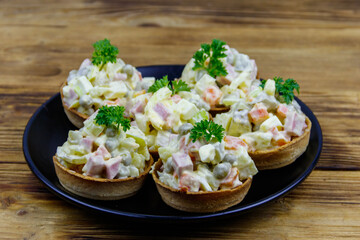 Traditional Russian festive salad Olivier in tartlets on wooden table
