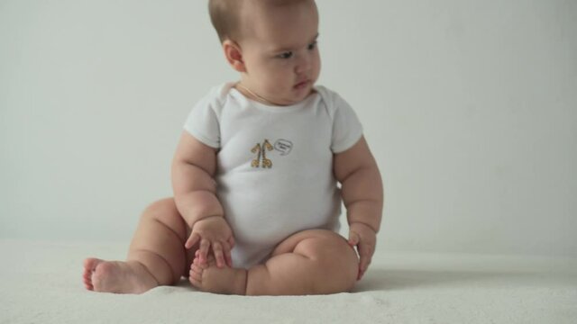 infant, childhood concept - happy funny playfull toddler kid 8 month baby girl learn to sit singly play on bed. smiling chubby active awake newborn crawl on knees indoors at home on white background