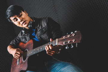 Asian male playing jazz with an acoustic guitar, place headphones on his neck for listening real sound in studio. Rehearsal and recording studio. Performance and show in the music business.
