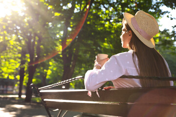 Woman with drink in park on sunny day, back view. Space for text