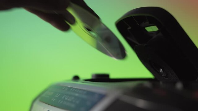 A man takes out a laser CD disk from an old music player on a green background. Hand close up. Retro technique. Previous generation of audio systems