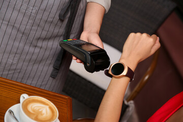 Woman making payment with smart watch in cafe, closeup