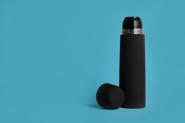 Stylish thermo bottle on light blue background, space for text