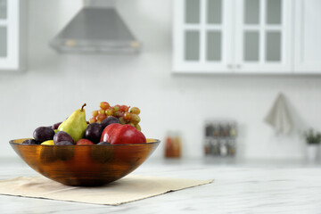 Different fresh fruits in bowl on white kitchen table. Space for text