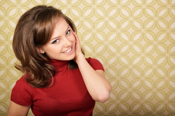 Young smiling ecstatic woman looking out at camera in room with vintage wallpaper, retro...