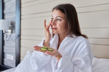 Mature female in bathrobe doing home spa treatments with cucumbers