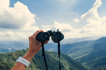 Hands holding binoculars on mountains forest nature background, looking through binoculars, travel,...