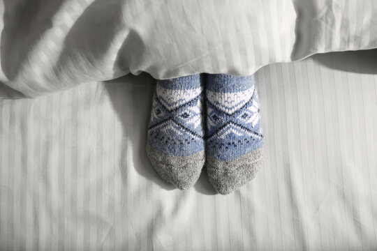 Woman wearing knitted socks under blanket in bed, top view