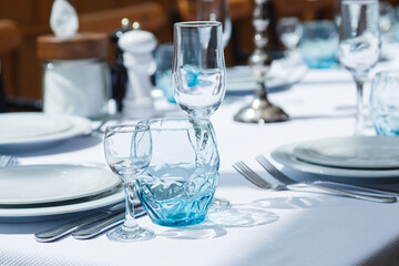 Festive table set, catering with white cloth, plates, forks, blue glasses, salt and pepper pots for wedding, family event or happy birthday party.