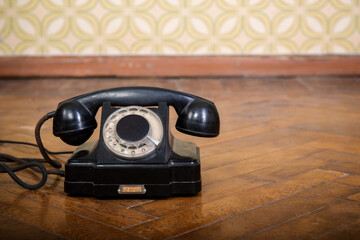 Retro black telephone is on the parquet floor against vintage wallpaper, detail interior 60-70ies...