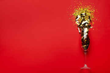 Flat lay composition with confetti and champagne glass on red background. Space for text