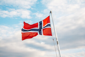 Norway flag on a background of blue sky with clouds. Space for your text message or promotional content