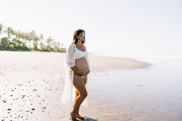 Fototapeta premium Relaxed young pregnant woman enjoying sunny day on sandy seashore