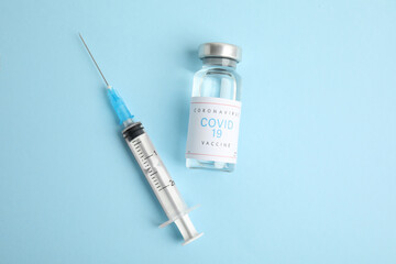 Vial with coronavirus vaccine and syringe on light blue background, flat lay