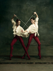 Contrast. Two young female ballet dancers like duelists with swords on dark green background. Caucasian models dancing together. Ballet and contemporary choreography concept. Creative art photo.
